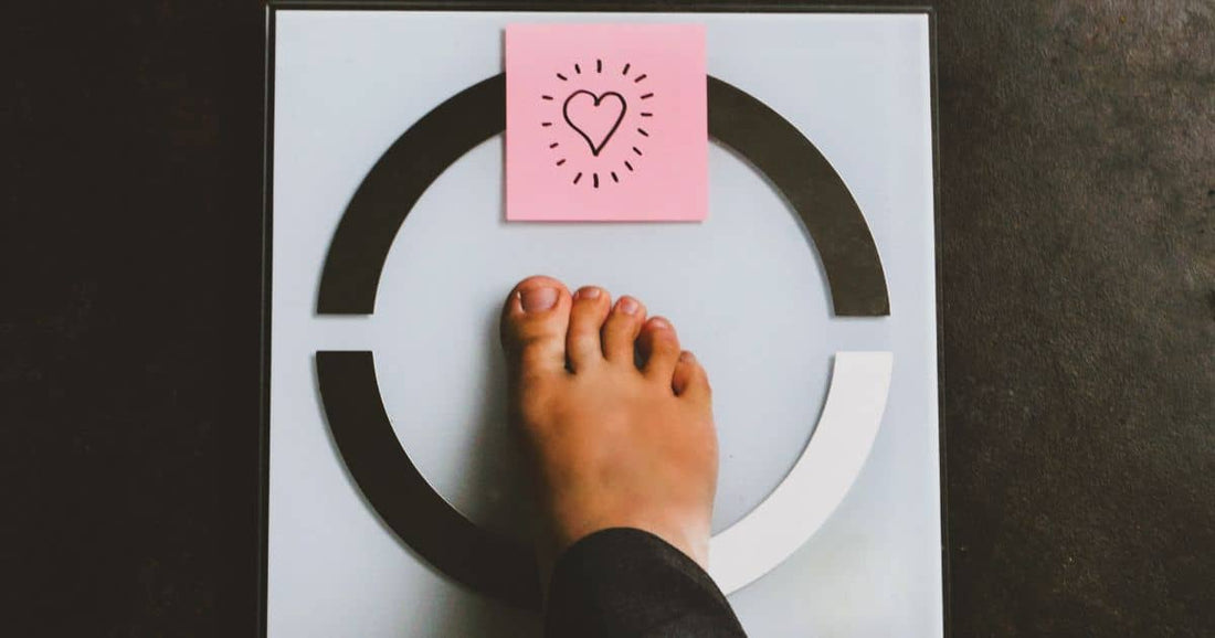 Foot on scale with heart sticky note symbolizing weight loss.